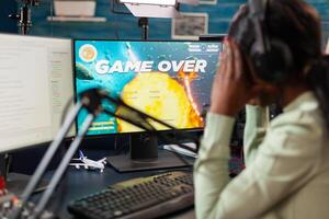 African esport player losing virtual tournament during live stream covering face. Professional gamer streaming online games with new graphics on powerful computer. photo
