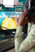 Afro esport player suffering lose defeat during space shooter live tournament. Professional gamer streaming online games with new graphics on powerful computer. photo