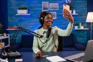 African influencer talking a selfie for listener while recording vlog. On-air online production internet podcast show host streaming live content, recording digital social media. photo