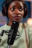 African host of online show using microphone talking with listeners entertainment. Speaking during livestreaming, blogger discussing in podcast wearing headphones. photo