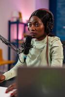 African influencer answering questions while talking into microphone for listeners. Speaking during livestreaming, blogger discussing in podcast wearing headphones. photo