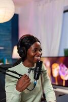 Cheerful creative vlogger recording podcast using production station in home studio. Speaking during livestreaming, blogger discussing in podcast wearing headphones. photo