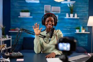 African blogger waving at audience while filming podcast. On-air production internet broadcast host streaming live content, recording digital social media photo
