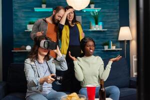 Multi ethnic friends losing online games compettion experiencing virtual reality with headset. Mixed race group of people hanging out together having fun late at night in living room. photo