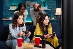Multi ethinc friends cheerful group of people relaxing on console games with controller. Group of mixed race friends playing games while sitting on sofa in living room late at night. photo