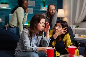 Woman upset after lose at online games while having socializing with multi ethnic group of friends in home living room late at night, drinking beer. photo