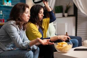 Multi ethnic friends upset after losing virtual reality gaming competition sitting on couch. Mixed race group of people hanging out together having fun late at night in living room photo