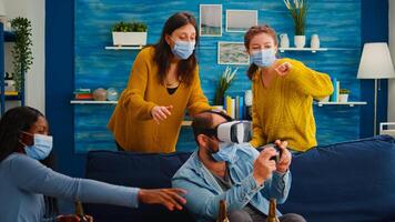 Group of multi ethnic friends with face mask enjoying playing games using vr headset goggles in living room keeping social distancing agaist covid19. Diverse people having fun at new normal party photo