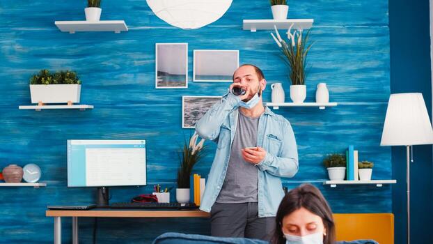 Man with standing in background texting on smartphone taking off protection mask drinking beer reading news waiting to start new normal party. Keeping social distancing against global pandemic photo