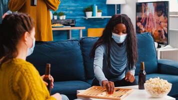 Group of cheerful multiethnic friends playing board games backgammon board games keeping social distancing wearing face mask to prevent infection with covid19 during global pandemic drinking beer photo