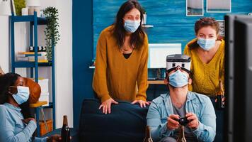 Mixed raced friends having fun playing game competion experiencing virtual reality keeping social distancing wearing masks to prevent sickness with covid. Diverse people in new normal party photo