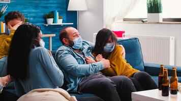 Group of multiethnic friends watching a horror movie on tv being afraid, spending weekend together wearing face mask to prevent infection with covid 19 during global pandemic enoying beer and chips photo