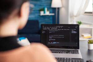 Young programmer writing virtual program code for software development and mobile application on laptop computer, Student programming javascript while sitting at desk table in living room photo