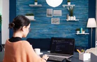 Back view of student developer writing javascript using analytic program while sitting at desk table in living room. Freelancer software developer programer programming digital code photo