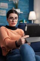 Portrait of student looking at tablet computer, sitting on sofa in living room drinking coffee. Teenager studying social communication using university digital app on mobile device photo