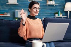Young woman greeting her teacher during virtual videocall meeting talking about university project. Student in living room on online internet web conference duting virtual e-learning class photo
