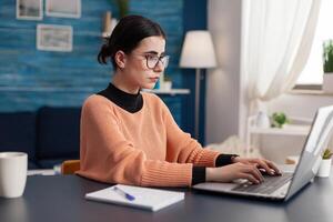 Teenager college studying management communication for university typing information on keyboard using laptop computer. Woman looking at e-learning platform while sitting at desk photo