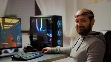 Portrait of happy man looking at camera smiling playing online FPS shooter videogame for virtual tournament. Cyber performing on powerful computer with RGB keyword during championship at home photo