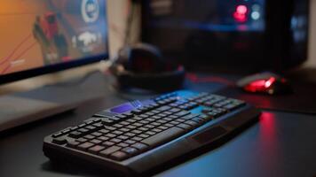 Close up of professional RGB keypad in empty gaming room prepared for streaming online tournament, display with first person shooter playing on it. Game studio with powerful computer photo
