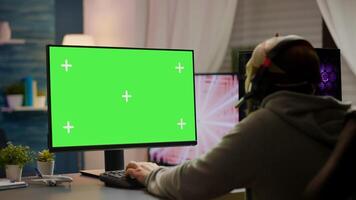 Professional cyber gamer playing games with greenscreen, chroma key, mock up desktop isolated display. Player using powerful computer with mockup screen streaming shooter games wearing headset photo