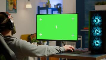 Pro gamer streaming games with green screen mock-up display in gaming home studio. Player using RGB professional computer with chroma key isolated desktop playing shooter games wearing headset photo