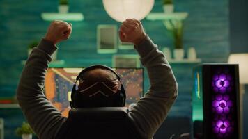 Back shot of happy gamer winning first person shooter game playing online on RGB powerful personal computer raising hands. Pro cyber performing during virtual tournament using technology network photo