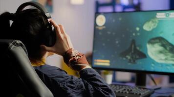 Focused woman gamer sitting on desk, putting on headset with a mic and starts playing space shooter game. Online streaming cyber performing on powerful personal computer during gaming tournament photo