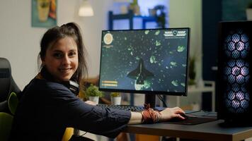Woman gamer with headset looking at camera smiling and playing virtual shooter game championship in cyberspace, esports player performing on powerful computer in stylish room during gaming tournament photo