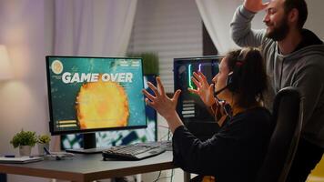 Stressed couple gamers losing space shooter game playing on RGB powerful computer while streaming online competition. Pro cyber woman with headset performing from home during virtual tournament photo