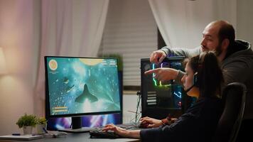 Man gamer teaching his girlfriend playing space shooter game on RGB powerful personal computer. Pro cyber woman with headset performing games streaming from home during online tournament photo