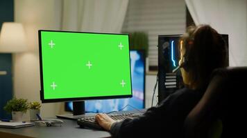 Pro gamer playing virtual game on powerful computer with green screen mock up, chroma key display. Cyber player using professional pc with isolated desktop streaming shooter games wearing headset photo