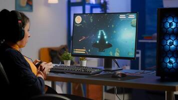 Addicted lady playing space shooter game using headphones ,wireless joystick and RGB powerful personal computer. Cyber gamer with headset and joypad performing virtual games at gaming championship photo