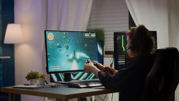 Back view shot of excited woman gamer streaming online games and wining playing on RGB powerful computer using wireless controller. Player with headphones celebrating victory in gaming room photo
