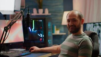 Streamer man looking at camera smiling while streaming videogames using stream chat. Pro cyber videogamer playing space shooter game at RGB powerful personal computer in gaming home studio photo