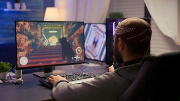 Back view of pro man gamer sitting on gaming chair at desk and playing first person shooter games at powerful computer. Digital gamer streaming online gameplay tournament with RGB neon lights photo