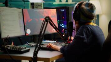 Streamer playing FPS videogames and talking with team mates on streaming open chat using professional microphone. Cyber performing in online tournament on RGB powerful computer in gaming sudio room photo
