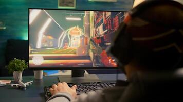 Back shot of pro esport gamer playing first person shooter game on powerful computer using RGB keyboard. Competitive player man streaming online game for tournament using professional equipment photo