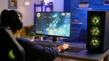 Gamer playing space shooter game on powerful computer using RGB gaming equipment. Pro player wearing headphones during digital esport tournament late at night at home studio. photo