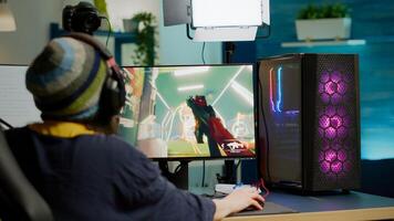 Back shot of pro streamer with headphone playing FPS videogame during esport competition using RGB powerful computer. Player sitting on gaming chair using streaming equipment late night in home studio photo