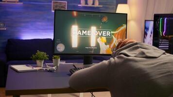 Over shoulder shot of man after losing at games on computer using professional RGB equipment. Defeted player playing first person shooter games using modern technology network wireless photo