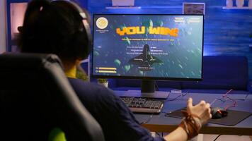 Excited pro gamer with professional headphones making winner gesture while playing space shooter games. Player streaming digital games during online competition using RGB system desktop photo