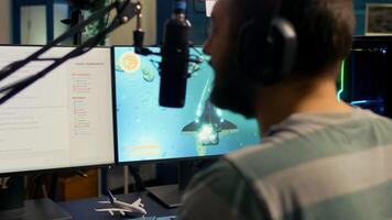 Back shot of streamer man playing on powerful computer shooter game for tournament, talking with multiple players into headphones. Pro game r using professional streaming equipment photo