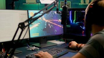 Pro gamer playing space shooter online games using RGB keyboard and mouse during virtual championship. Streamer looking into monitors, talking with team on streaming chat photo