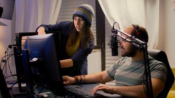 Girlfriend supports her pro gamer boyfriend, playing online game using streaming professional equipment. Streamer talking into microphone with multiple players during gaming tournament photo