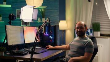 Streamer man looking at camera and smiling while streaming chat is open. Videogamer streamer playing space shooter game at gaming home studio equipped with professional equipment photo