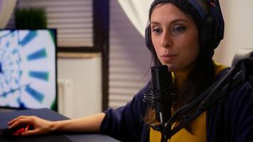 Streamer puts her headphone and start talking into microphone with other players during online game professional competition. Pro gamer sitting on gaming chair in streaming home studio with RGB photo