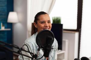 Woman blogger recording conversation with microphone in studio. Content creator hosting podcast for social media channel. Smiling influencer working with audio streaming equipment. photo