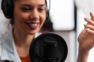 Closeup of woman influencer talking into microphone. Podcast presenter with headphones using recording equipment for live broadcast. Audio streaming for internet online radio production. photo