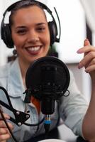 Closeup of smiling woman influencer talking into microphone. Vlogger with headphones using recording gear for live broadcast. Audio streaming equipment for internet online radio production. photo