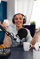 Portrait of smiling presenter streaming podcast using microphone. Social media influencer with headphones recording live stream on camera. Content creator live broadcasting in home studio. photo